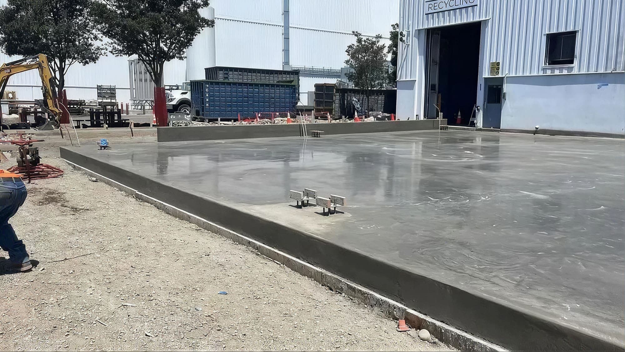 Large steel-troweled concrete equipment pad with anchor bolts set at an industrial recycling facility