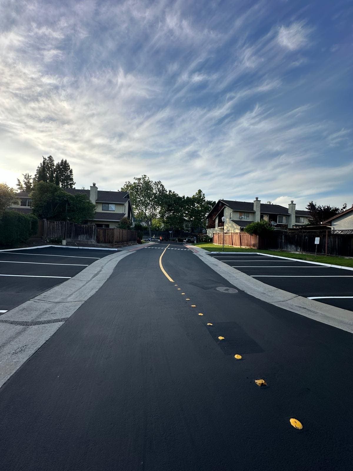 Newly paved residential roadway with fresh yellow centerline, raised markers, and striped parking bays