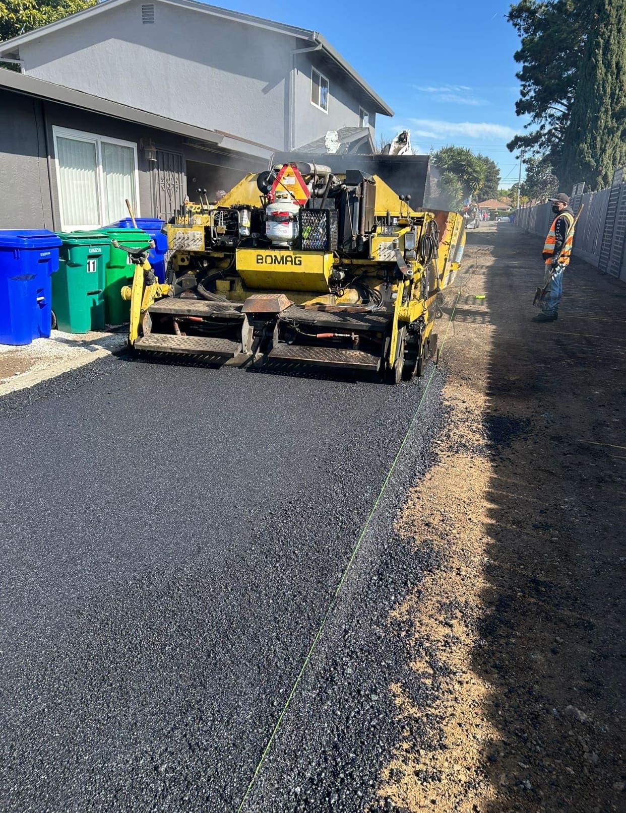 Asphalt paver placing hot mix along a residential drive with a Paragon crew member spotting the edge