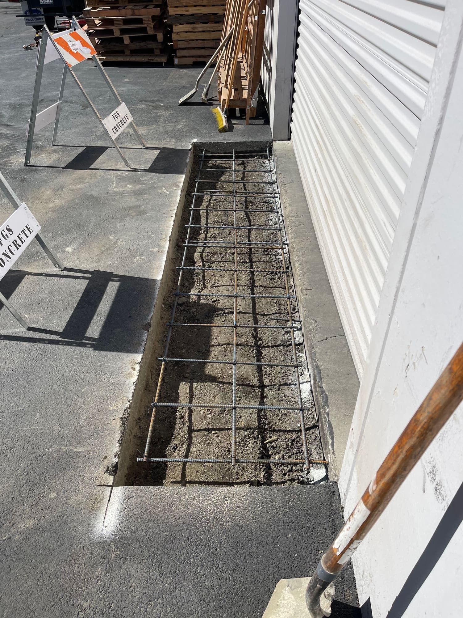 Excavated concrete footing with a tied rebar cage in place alongside a warehouse wall