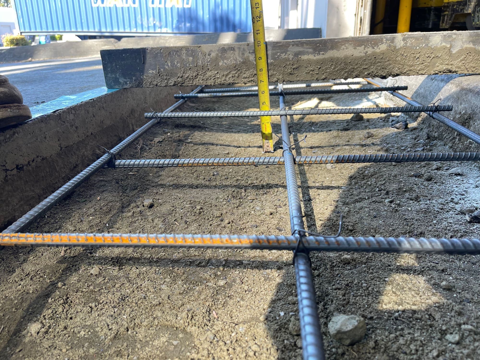 Tied rebar mat in a formed slab with a tape measure verifying depth before the concrete pour
