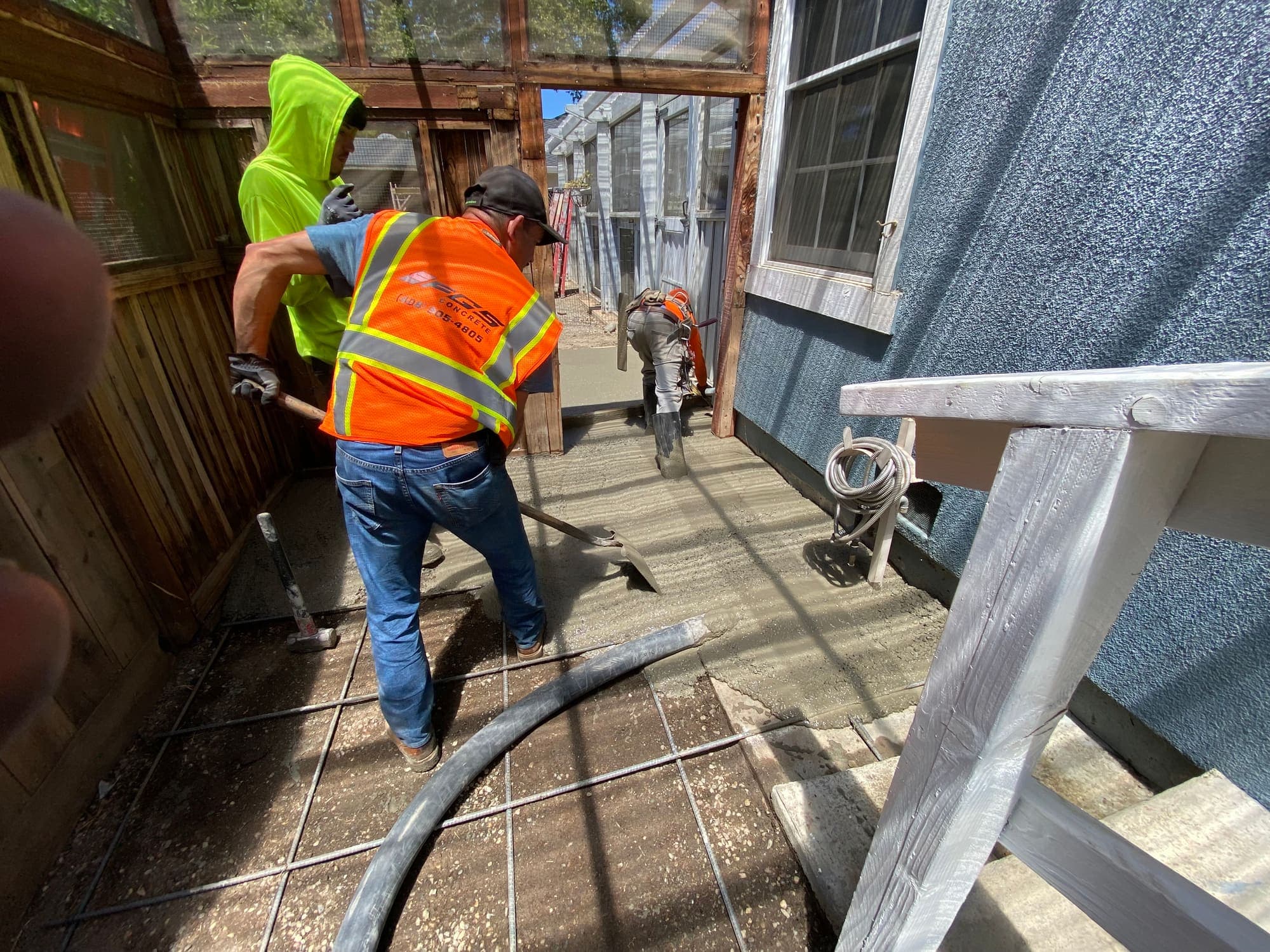 Two crew members screeding concrete in a narrow side-yard access where machinery cannot reach
