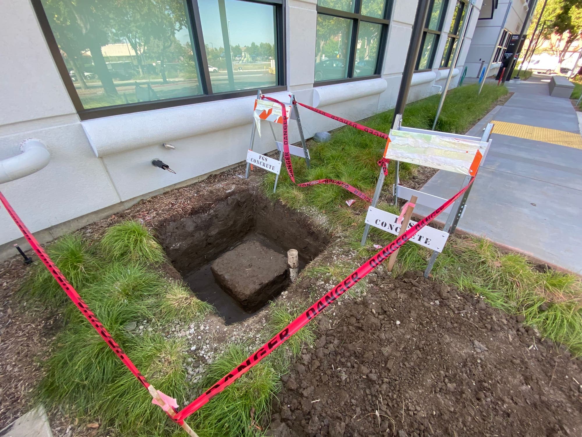 Open utility excavation in a landscaped area with marked locate lines and protective barricade tape