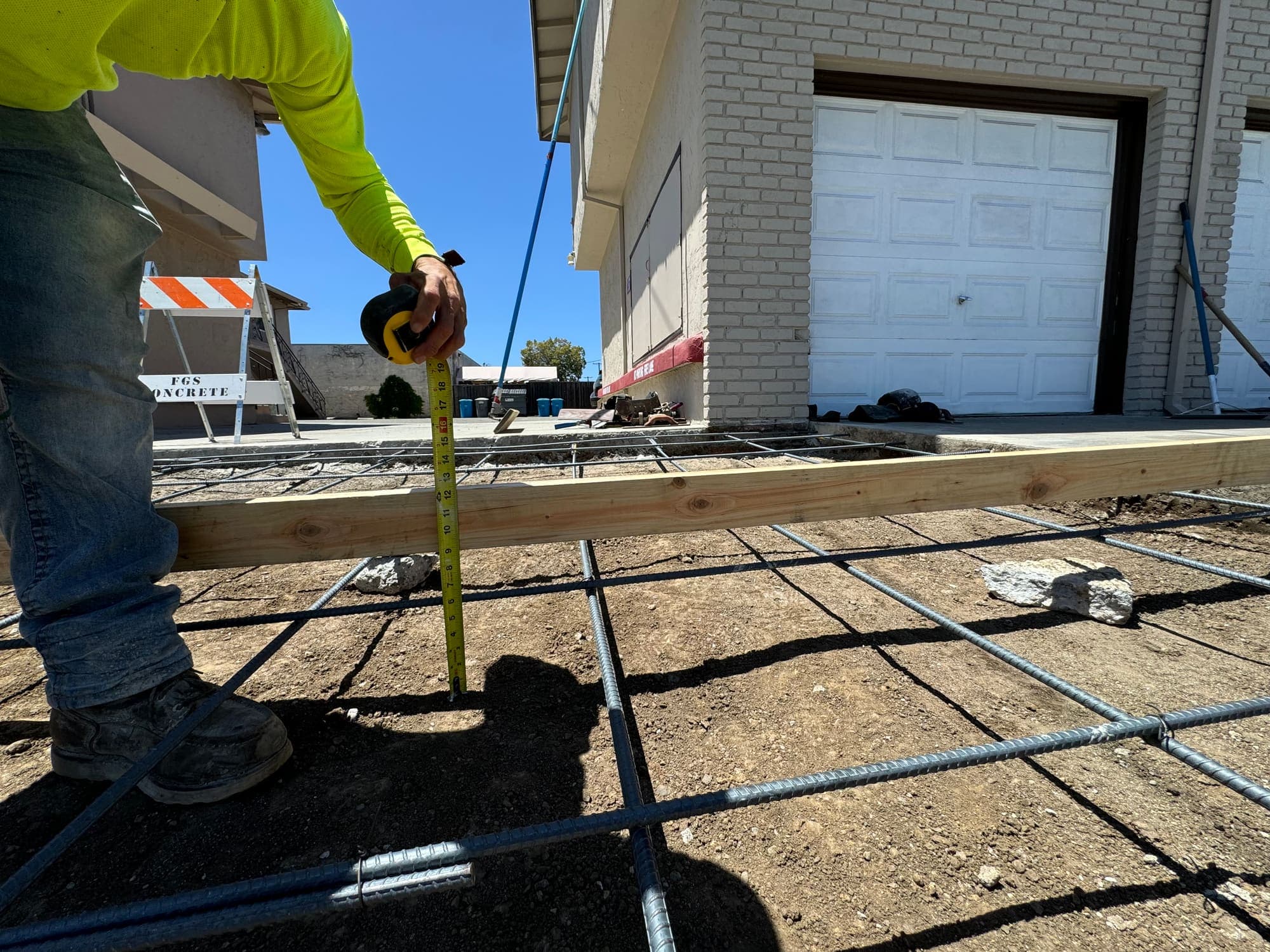Crew member measuring and tying rebar for a slab foundation against a commercial building