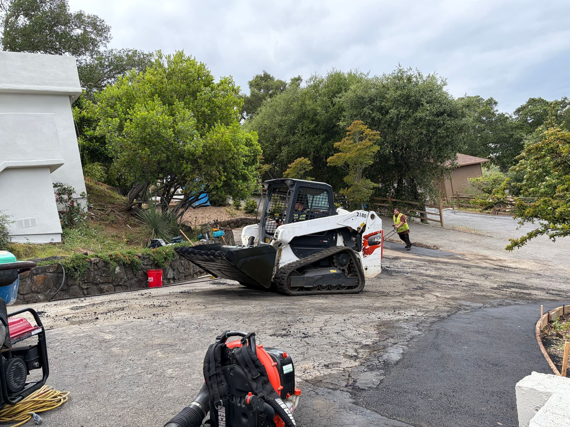 Skid steer removing failed asphalt and grading the base before repaving